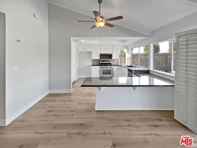 kitchen with kitchen peninsula, appliances with stainless steel finishes, sink, white cabinets, and lofted ceiling