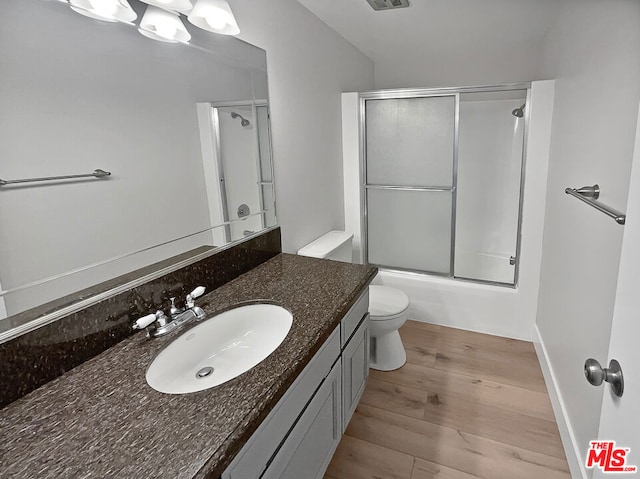 full bathroom with hardwood / wood-style flooring, vanity, toilet, and enclosed tub / shower combo