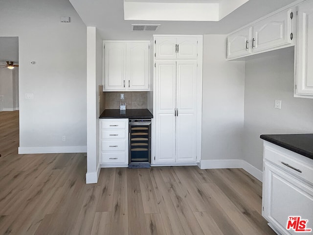 kitchen featuring white cabinetry, ceiling fan, wine cooler, decorative backsplash, and light wood-type flooring