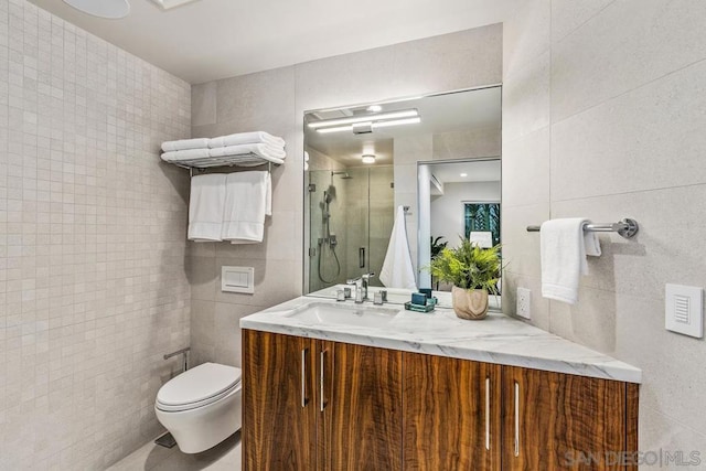 bathroom with vanity, toilet, a shower with door, and tile walls