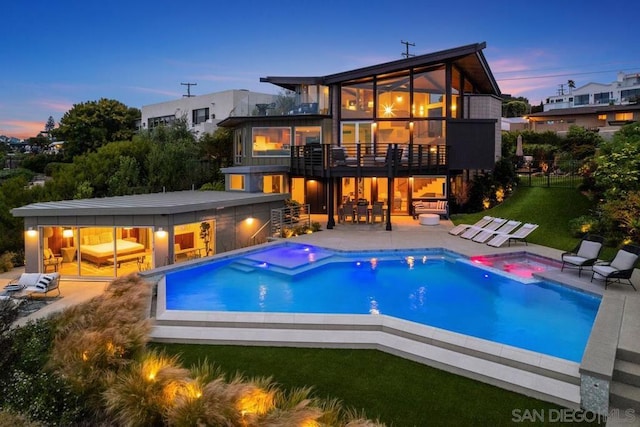 back house at dusk featuring a patio area, a balcony, a yard, and a swimming pool with hot tub