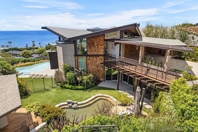 rear view of property featuring a patio area, a water view, a yard, and a fenced in pool