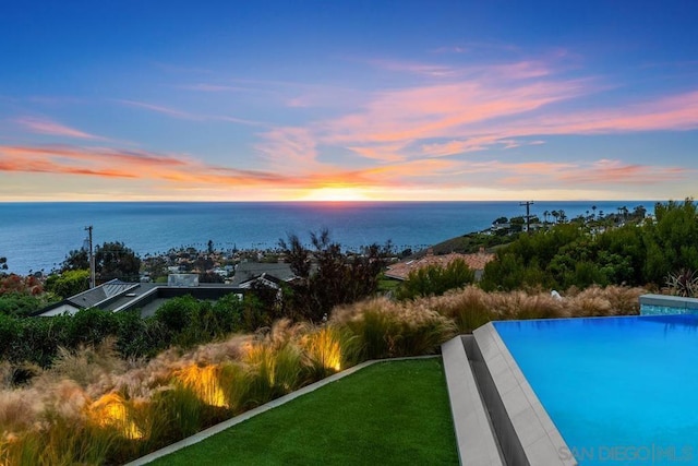 pool at dusk featuring a yard and a water view