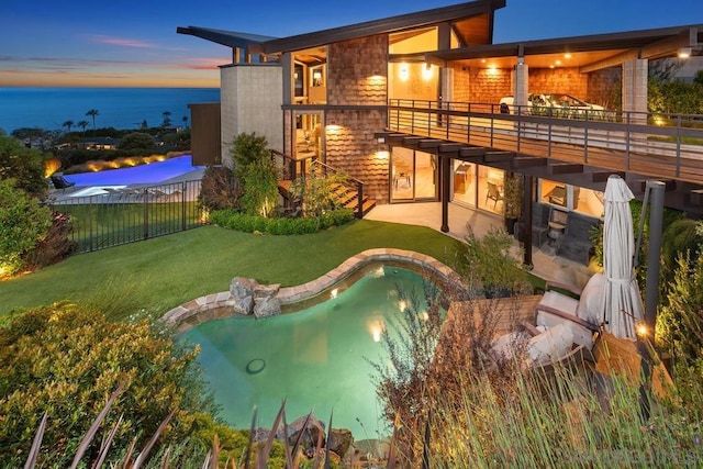 back house at dusk with a balcony, a yard, and a water view