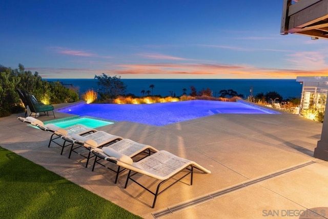 pool at dusk featuring a patio and a water view