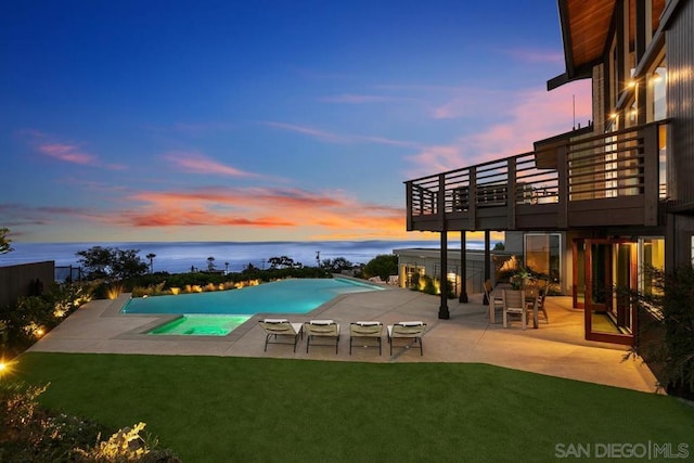 pool at dusk with a yard, a water view, and a patio area