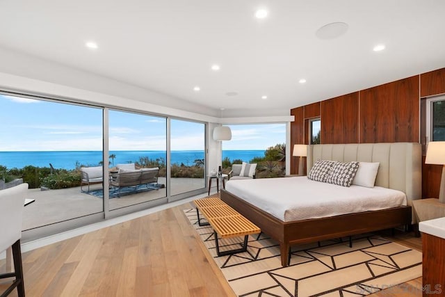 bedroom with access to outside, light wood-type flooring, a water view, and wooden walls