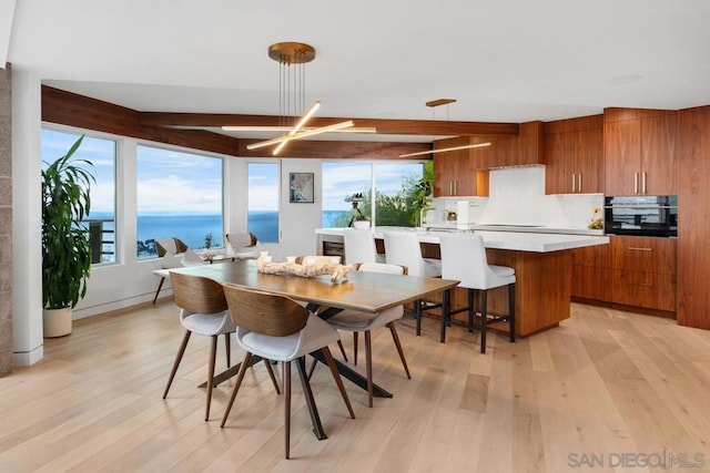 dining space featuring beamed ceiling, light wood-type flooring, and a water view