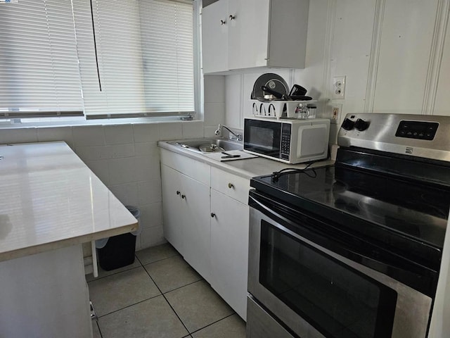 kitchen with white cabinets, light tile patterned floors, sink, and stainless steel electric range