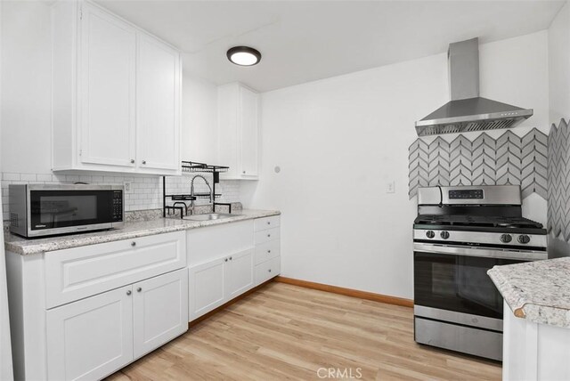 kitchen featuring wall chimney range hood, sink, light hardwood / wood-style flooring, stainless steel appliances, and white cabinets