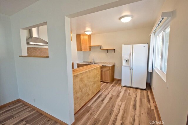 kitchen with light brown cabinetry, sink, light wood-type flooring, white refrigerator with ice dispenser, and wall chimney range hood