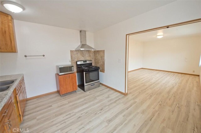 kitchen featuring wall chimney range hood, light hardwood / wood-style floors, sink, and appliances with stainless steel finishes