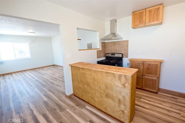 kitchen with wood counters, stainless steel gas range, light hardwood / wood-style floors, and wall chimney exhaust hood