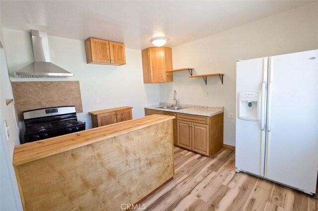 kitchen featuring stainless steel gas stove, sink, white fridge with ice dispenser, light hardwood / wood-style floors, and wall chimney exhaust hood