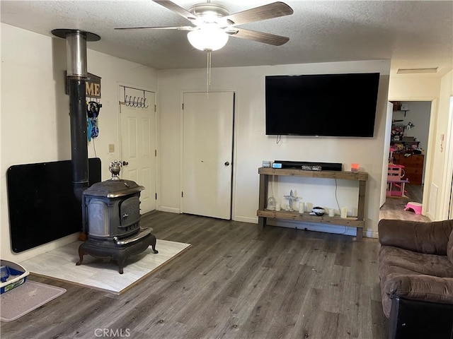 living room featuring hardwood / wood-style floors, a textured ceiling, a wood stove, and ceiling fan