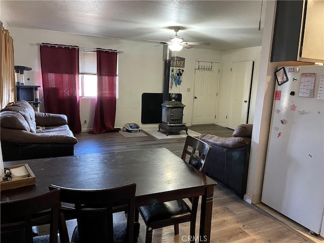 dining room with hardwood / wood-style flooring, ceiling fan, a wood stove, and a textured ceiling