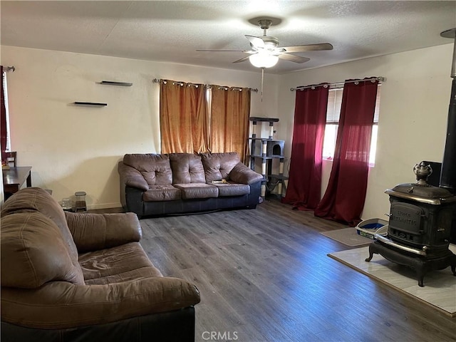 living room with hardwood / wood-style flooring, ceiling fan, a wood stove, and a textured ceiling