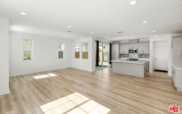 kitchen with a center island with sink, backsplash, sink, and light hardwood / wood-style flooring