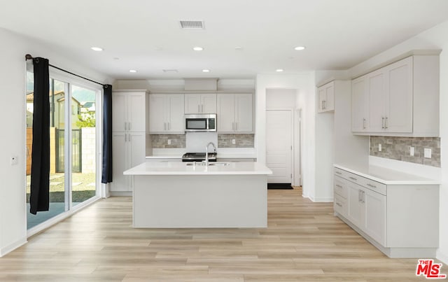 kitchen with tasteful backsplash, a kitchen island with sink, sink, white cabinets, and light hardwood / wood-style floors