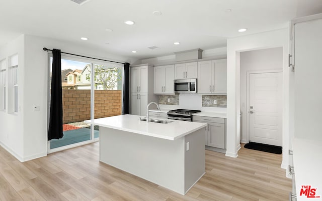 kitchen with decorative backsplash, appliances with stainless steel finishes, light wood-type flooring, a kitchen island with sink, and sink