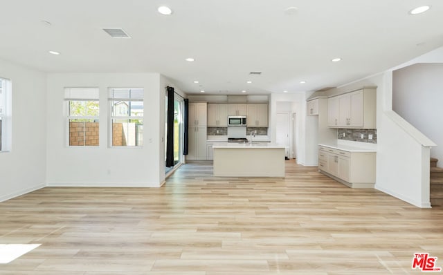 kitchen with tasteful backsplash, a center island with sink, light hardwood / wood-style floors, and sink