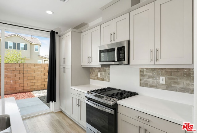 kitchen featuring decorative backsplash, light wood-type flooring, white cabinetry, and stainless steel appliances