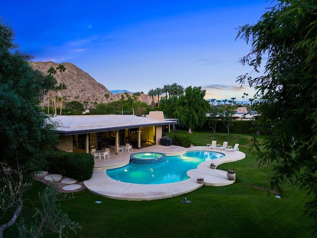 pool at dusk featuring a lawn, a patio area, an in ground hot tub, and a mountain view