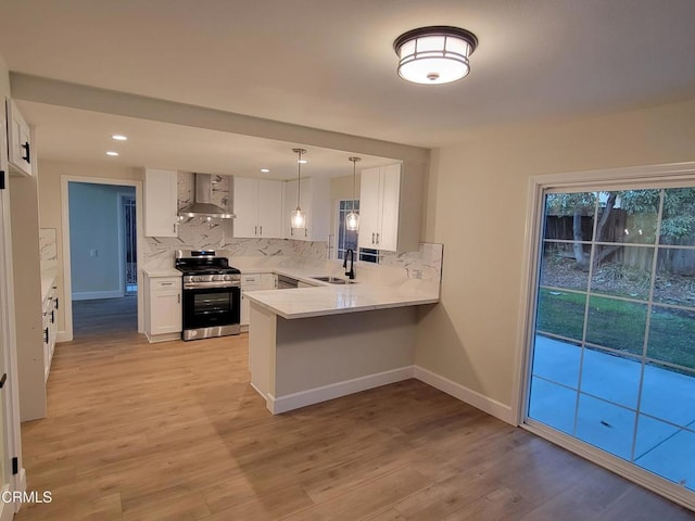 kitchen with kitchen peninsula, wall chimney exhaust hood, sink, white cabinets, and stainless steel stove