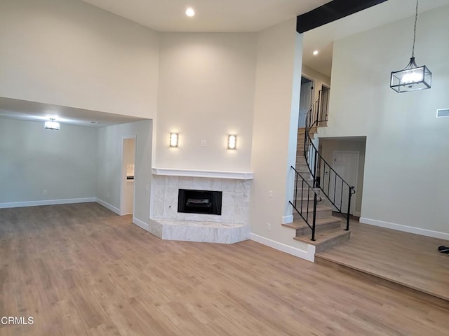 unfurnished living room with a tiled fireplace, a towering ceiling, and hardwood / wood-style flooring