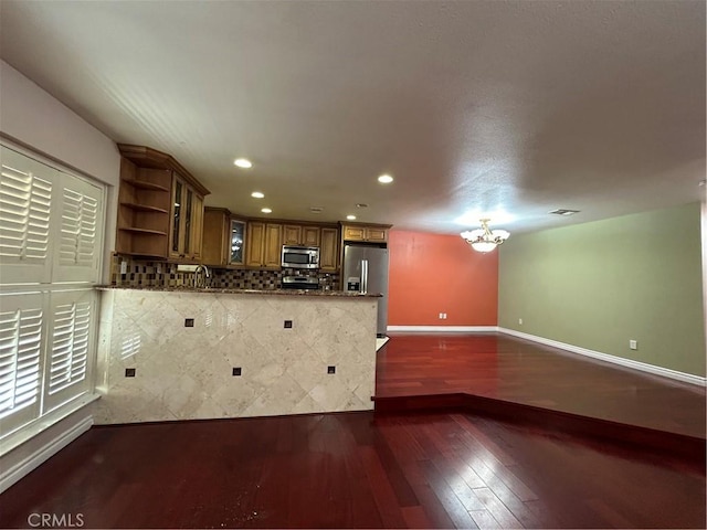 kitchen featuring stainless steel appliances, an inviting chandelier, dark hardwood / wood-style floors, kitchen peninsula, and dark stone countertops