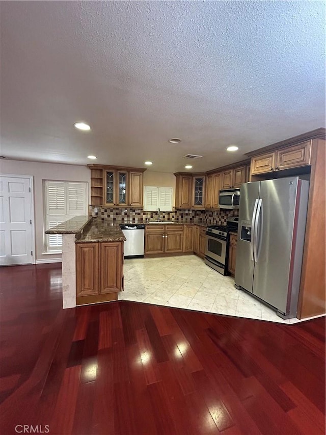 kitchen with backsplash, dark stone counters, sink, light wood-type flooring, and appliances with stainless steel finishes