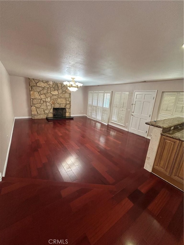 unfurnished living room featuring a textured ceiling, a stone fireplace, dark hardwood / wood-style floors, and a notable chandelier