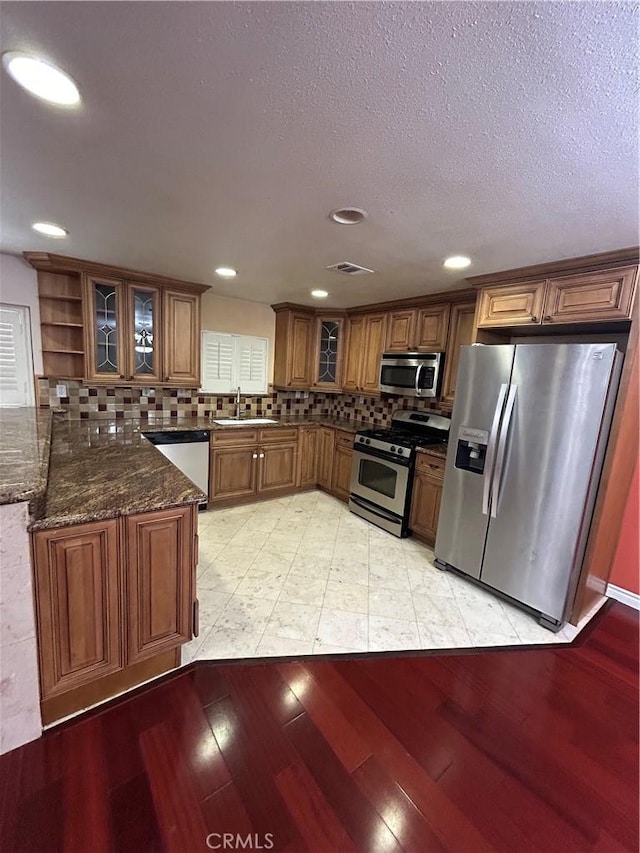 kitchen with appliances with stainless steel finishes, tasteful backsplash, sink, light hardwood / wood-style flooring, and dark stone countertops