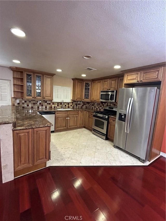 kitchen with sink, light hardwood / wood-style flooring, dark stone counters, decorative backsplash, and appliances with stainless steel finishes