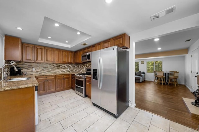 kitchen featuring stainless steel appliances, light stone countertops, a raised ceiling, light tile patterned floors, and sink