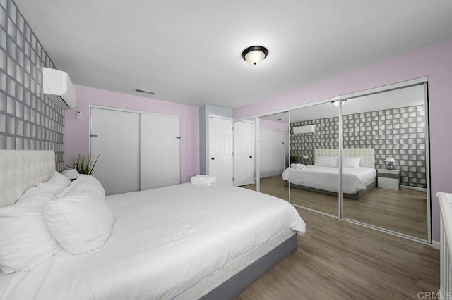 bedroom with an AC wall unit, multiple closets, and dark hardwood / wood-style floors