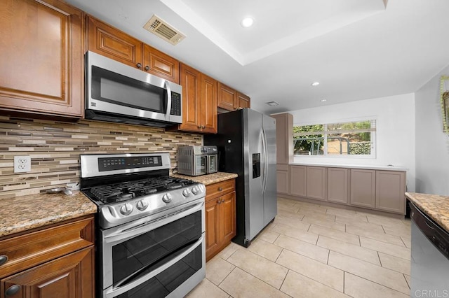 kitchen with backsplash, appliances with stainless steel finishes, light stone countertops, and a raised ceiling