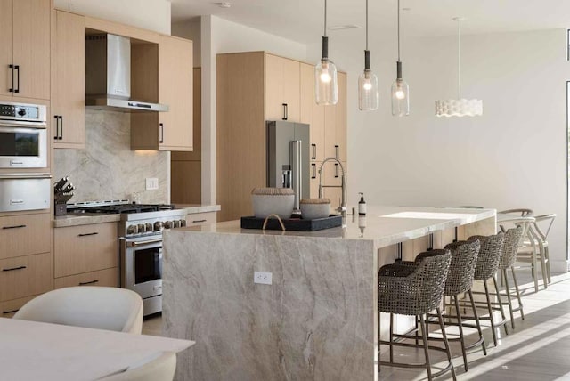 kitchen with light brown cabinets, a kitchen island with sink, wall chimney range hood, light hardwood / wood-style floors, and high quality appliances