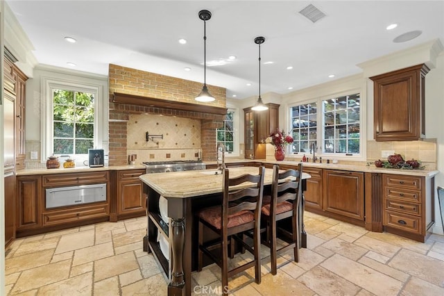 kitchen featuring a breakfast bar area, light stone counters, hanging light fixtures, a center island with sink, and backsplash