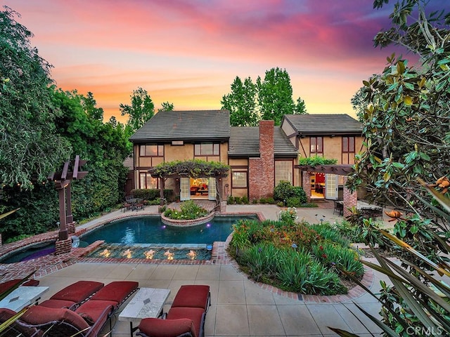 pool at dusk with a patio area and a hot tub