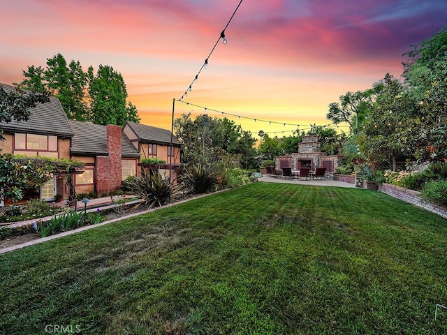 yard at dusk featuring a fireplace and a patio