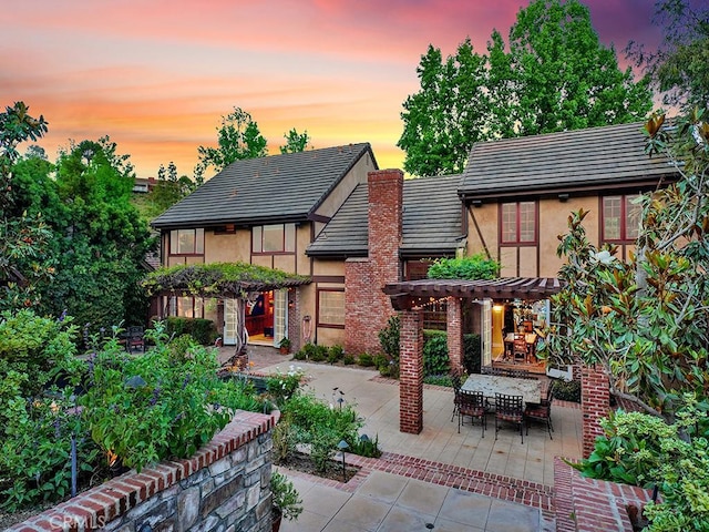 back house at dusk featuring a fireplace and a patio