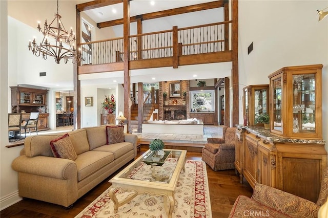 living room featuring dark wood-type flooring, a notable chandelier, a fireplace, and a towering ceiling