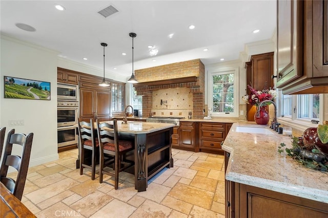 kitchen with an island with sink, sink, a kitchen breakfast bar, hanging light fixtures, and light stone counters