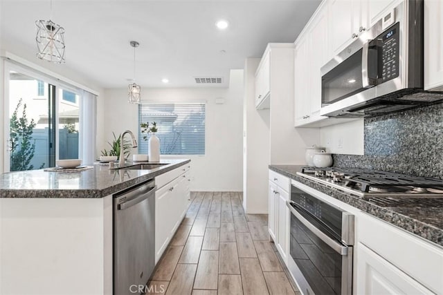 kitchen featuring pendant lighting, white cabinets, sink, an island with sink, and appliances with stainless steel finishes