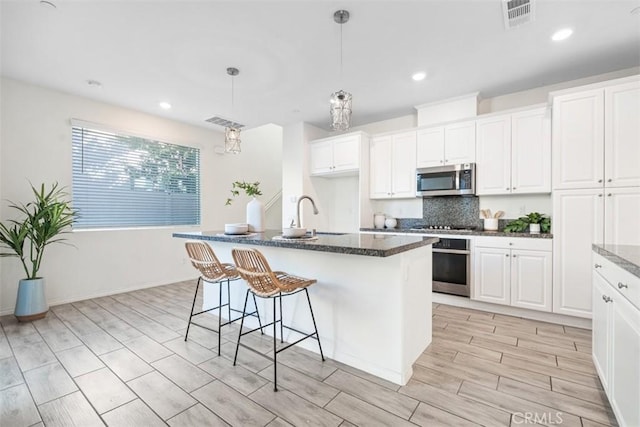 kitchen with white cabinetry, sink, stainless steel appliances, pendant lighting, and a center island with sink