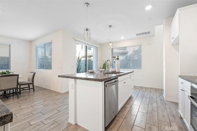 kitchen with hanging light fixtures, stainless steel dishwasher, an island with sink, light hardwood / wood-style floors, and white cabinetry