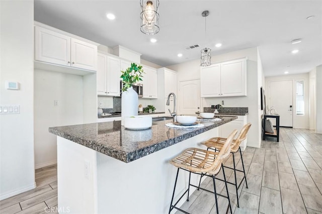 kitchen with a center island with sink, white cabinets, light wood-type flooring, and sink