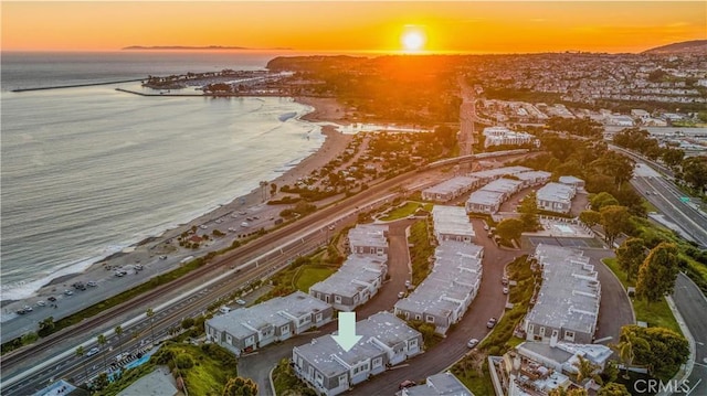 aerial view at dusk featuring a water view and a beach view