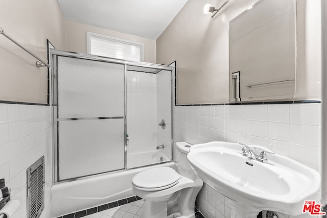 full bathroom featuring sink, tile patterned flooring, toilet, shower / bath combination with glass door, and tile walls